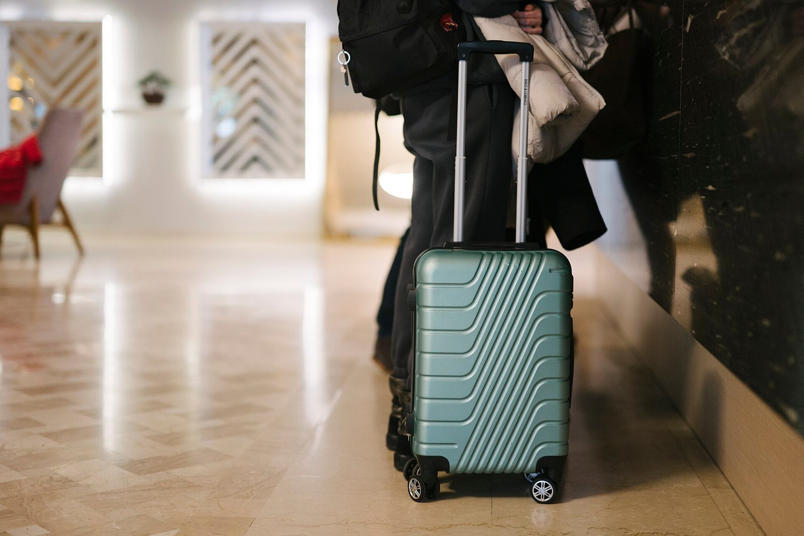 Traveler waiting in a bright hotel lobby beside a teal suitcase